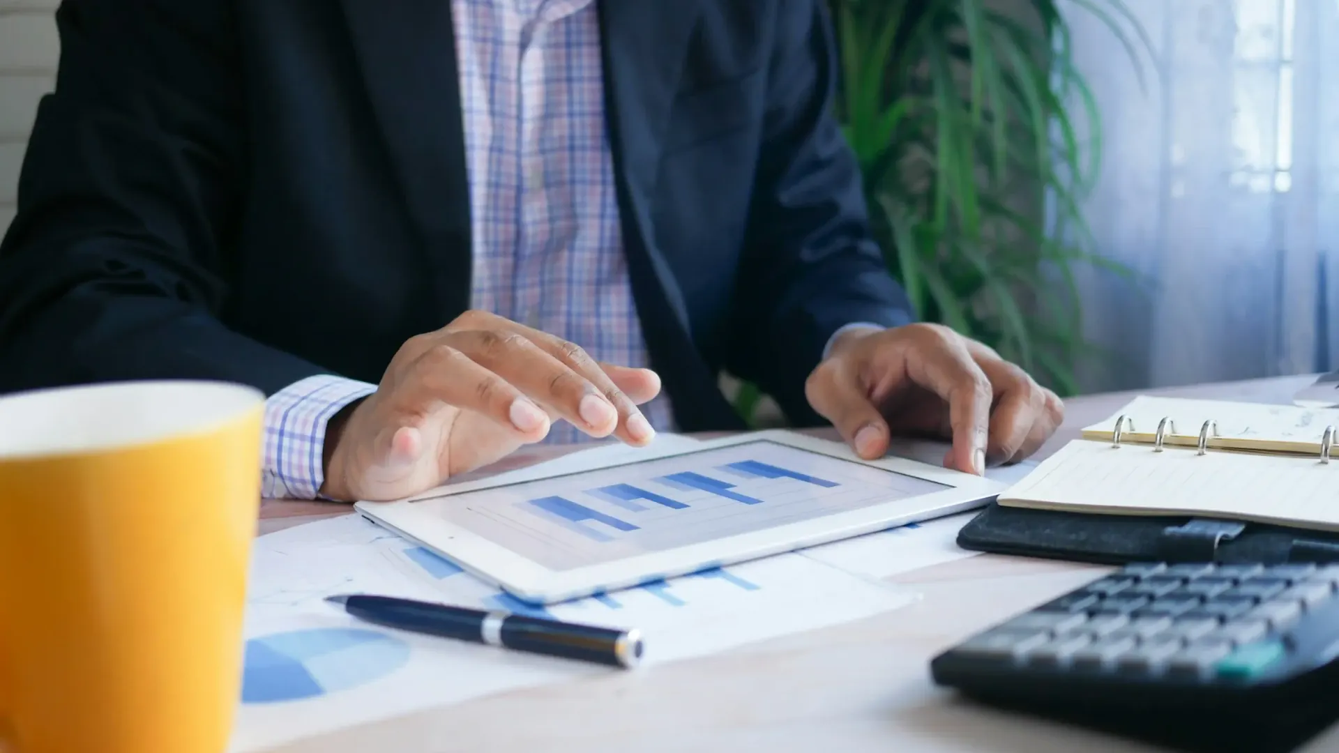 Contador revisando gráficas financieras en una tableta junto a una calculadora, estados de cuenta y notas de trabajo: contabilidad para personas físicas de Rodríguez Bravo y Asociados, con registro contable, cálculo de impuestos y cumplimiento ante el SAT.